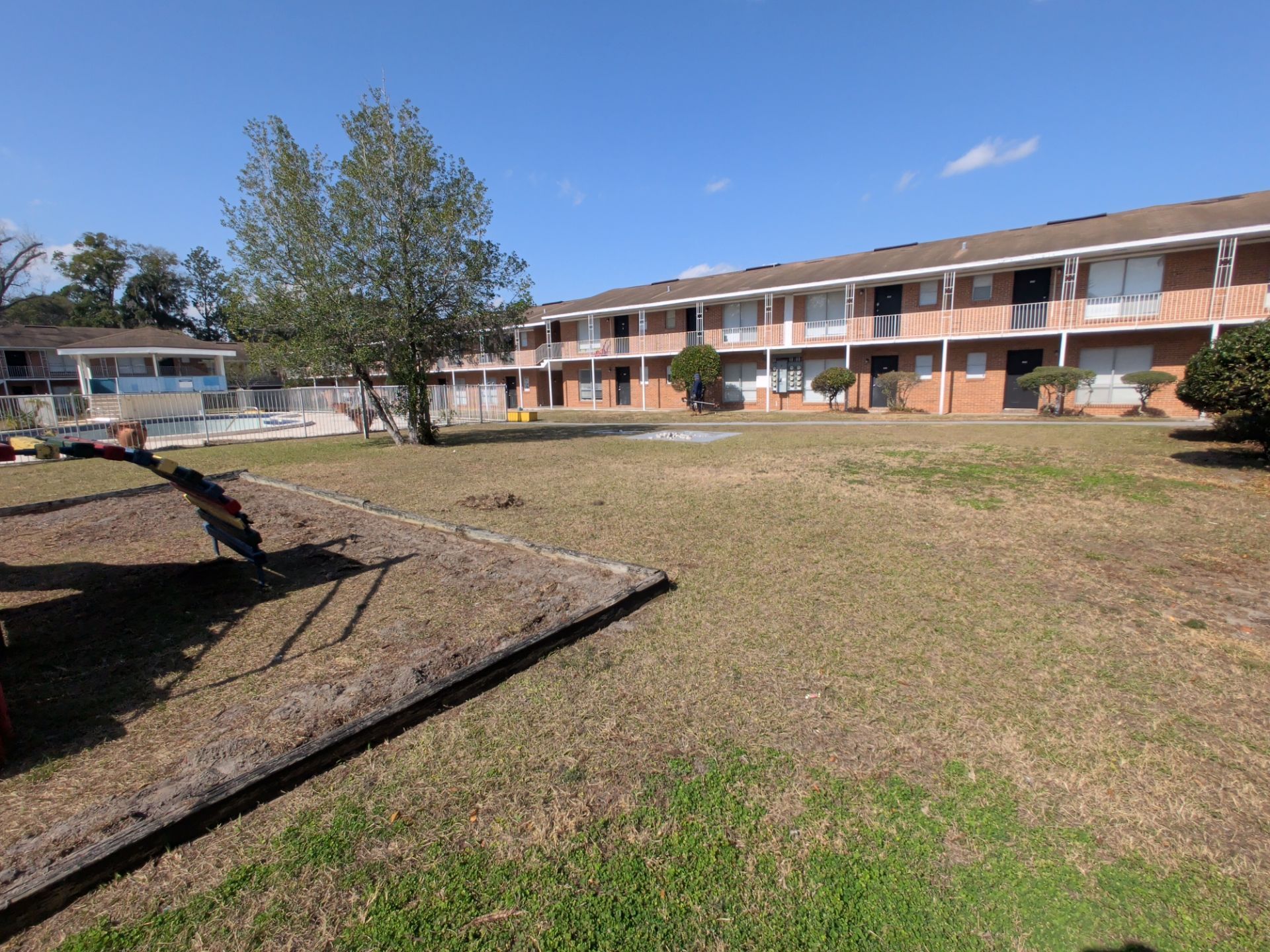 Apartment complex with a courtyard on a sunny day. Brown brick buildings, green grass, and a blue sky.