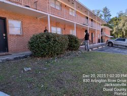 Person trimming bushes in front of a brick apartment building, Jacksonville, Florida.