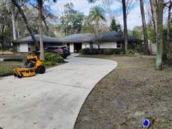 A house with a long driveway. A riding lawnmower is on the driveway.