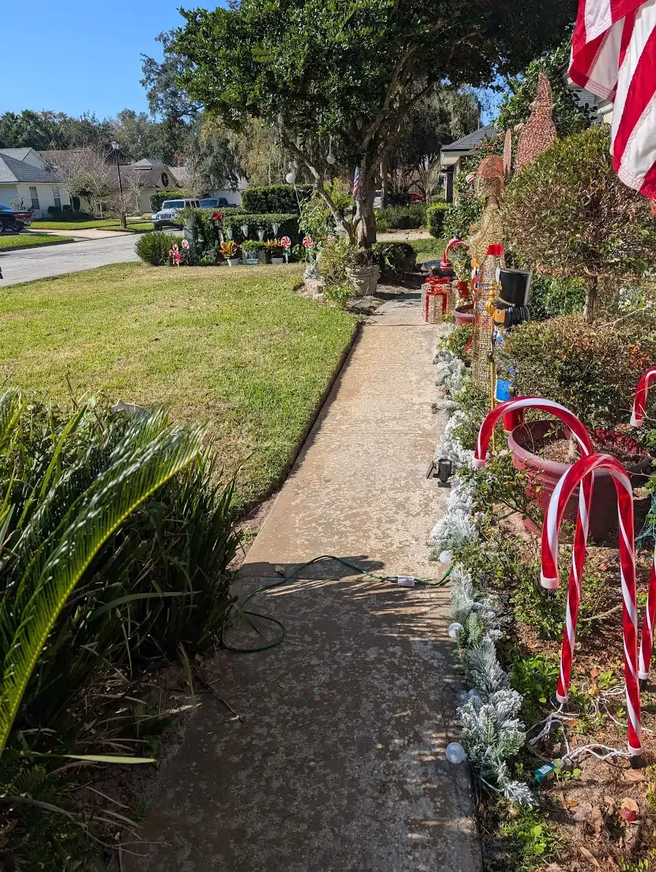 A concrete walkway leading towards a house with Christmas decorations; sunny day.