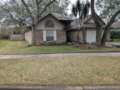 Brick house with a small lawn. Trees frame the house on the sides. Overcast day.