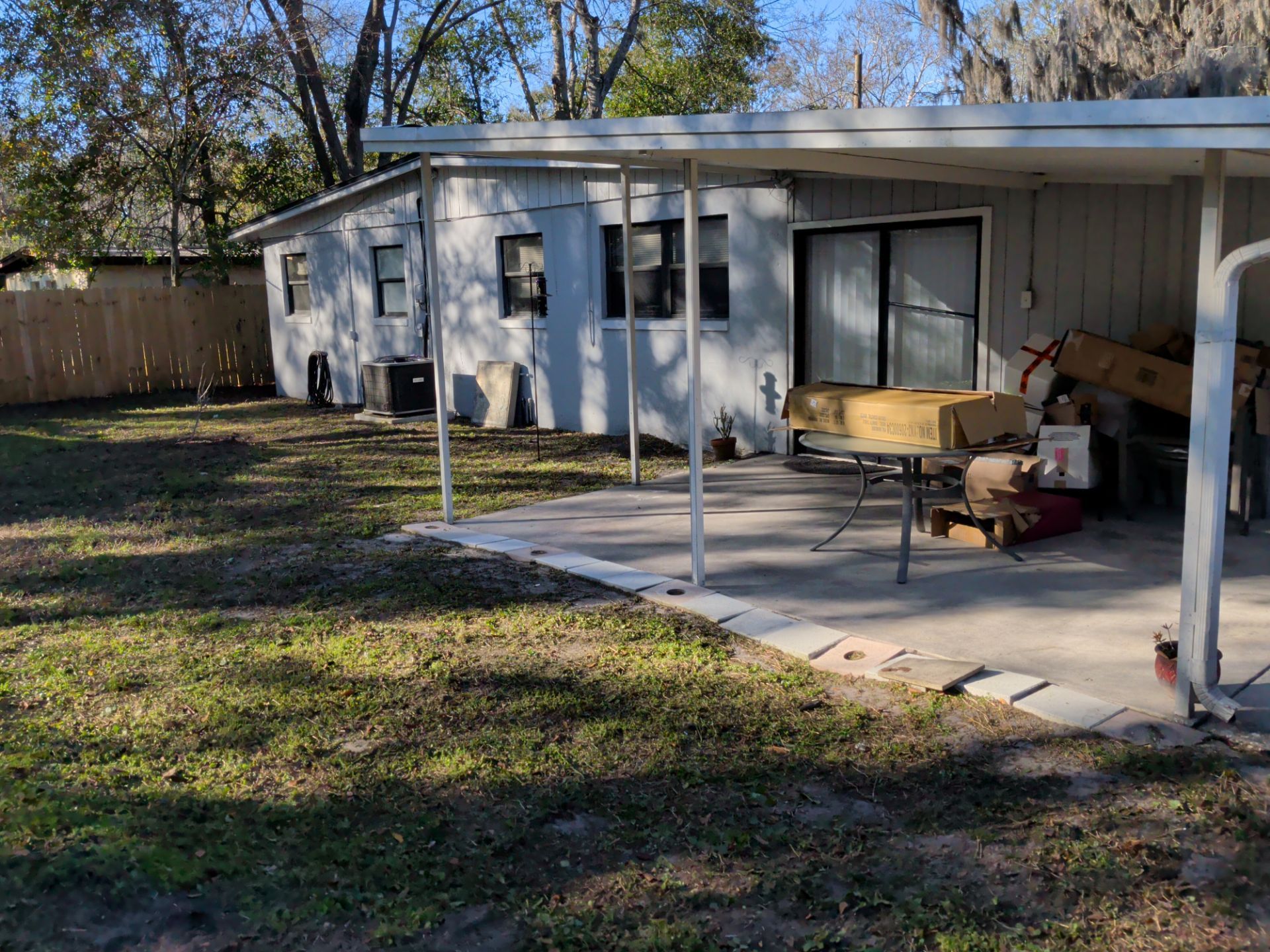 Backyard with a light gray house, a concrete patio under a white carport, and a wooden fence.