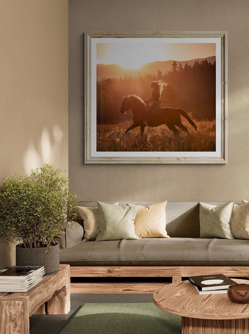 A framed photo of a person riding a horse at sunset. The room has a couch, plants, and coffee tables.