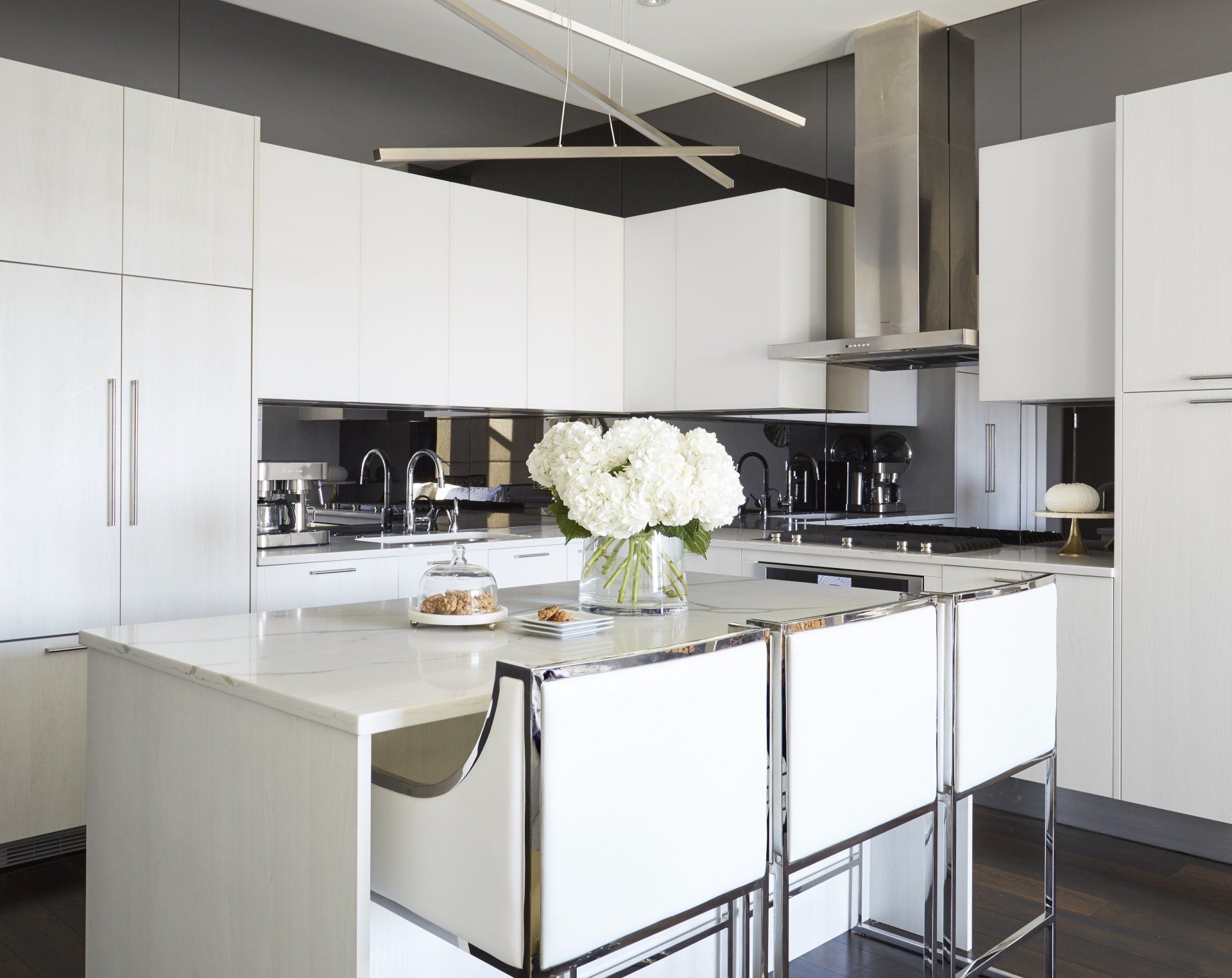A kitchen with white cabinets and stools and a vase of flowers on the counter.