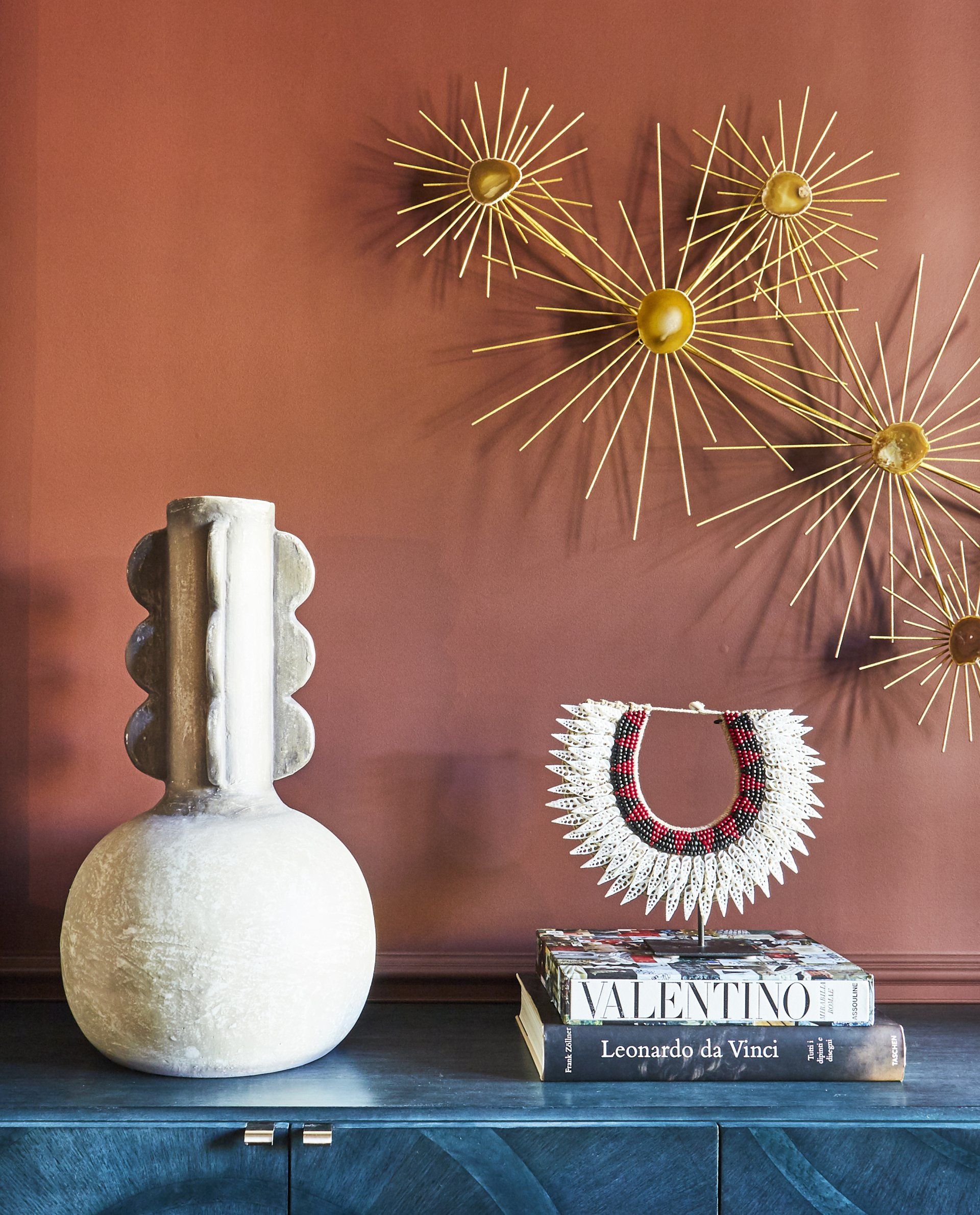 A vase and a necklace are on a table in front of a red wall.