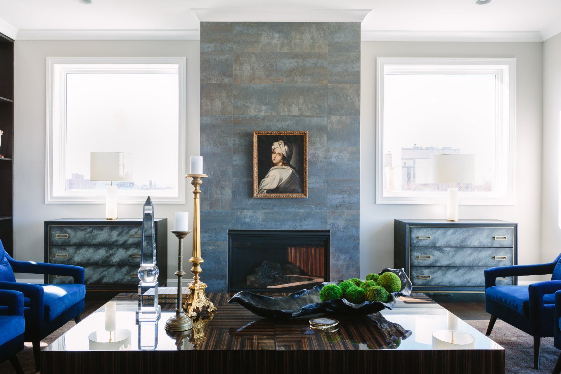A living room with a fireplace , two chairs , a coffee table and a painting on the wall.