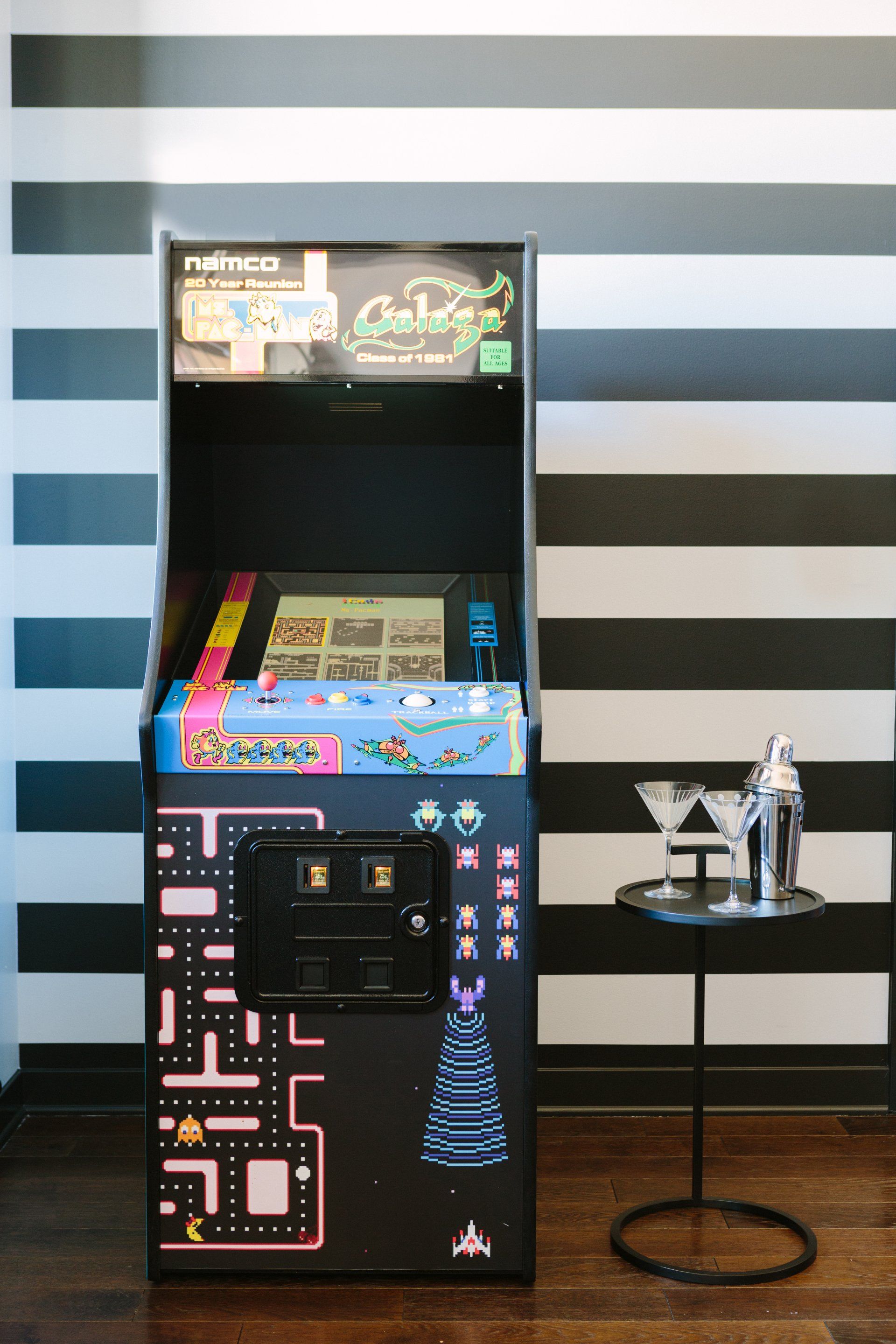 A pac man arcade game is sitting on a wooden floor in front of a black and white striped wall.