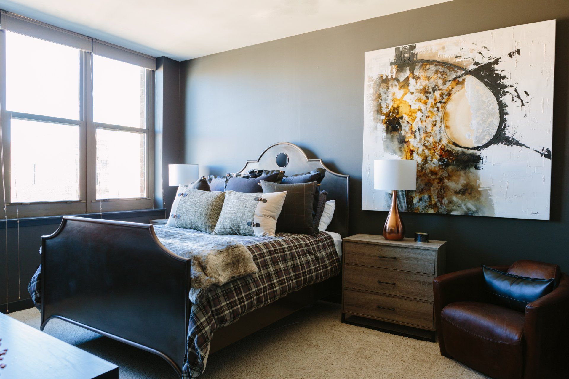 A bedroom with a bed , nightstand , chair and painting on the wall.