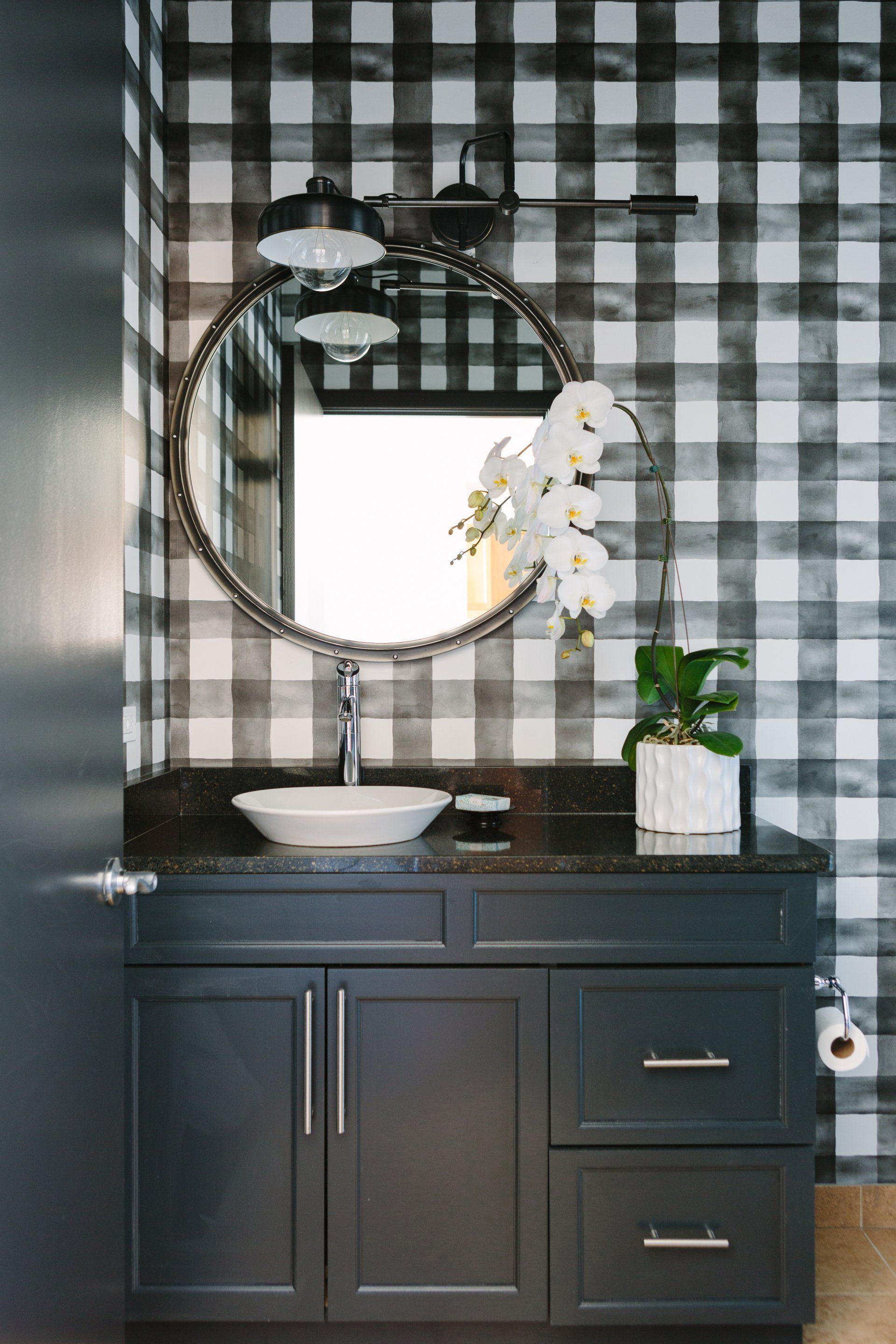 A bathroom with a sink , mirror , and plaid wallpaper.