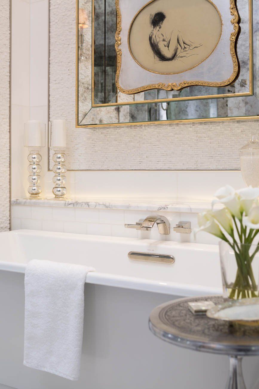 A bathroom with a bathtub , mirror , candles and a vase of flowers.