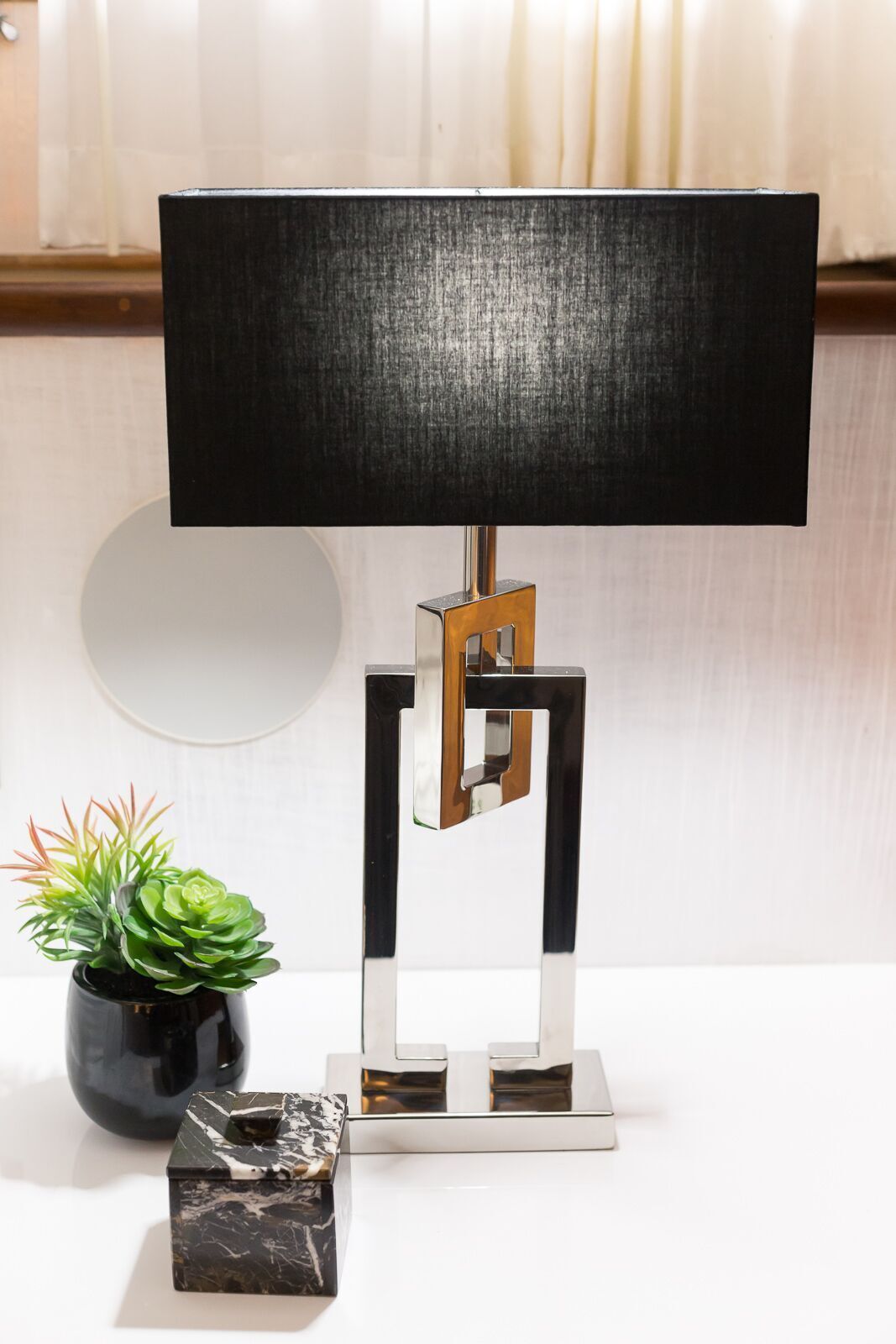 A lamp with a black shade is sitting on a table next to a potted plant.