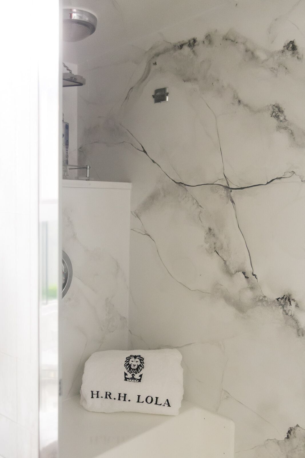A bathroom with a marble wall and a towel that says h.r.h. lola