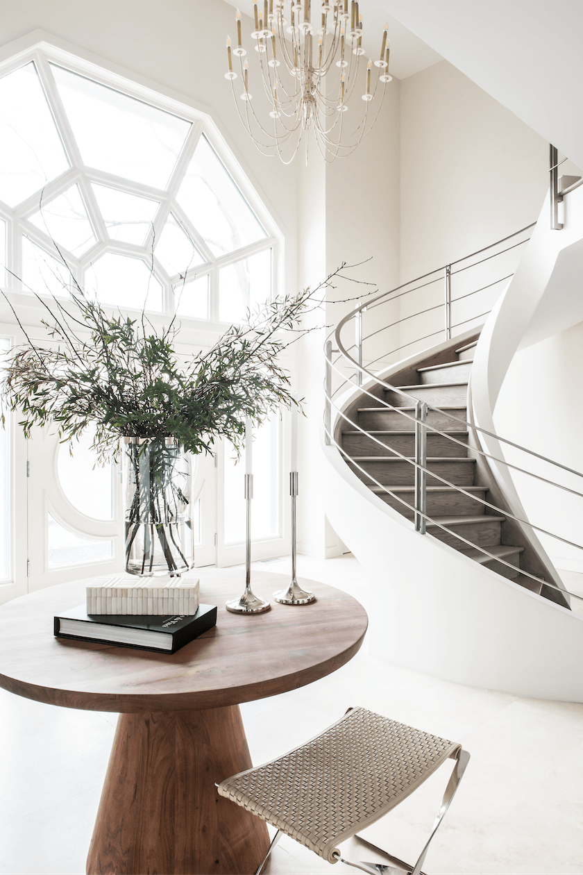 A wooden table with a vase of flowers on it in front of a spiral staircase.