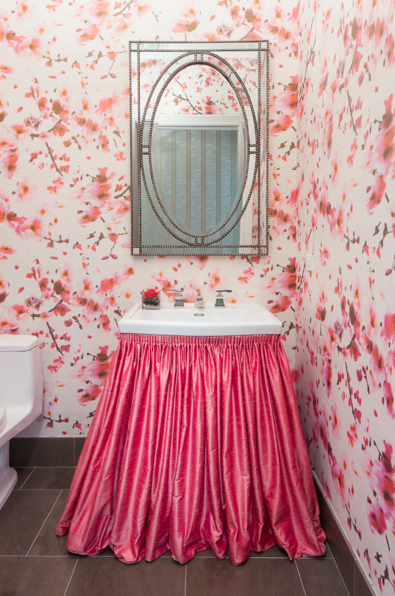 A bathroom with a sink covered in a pink skirt and a mirror.
