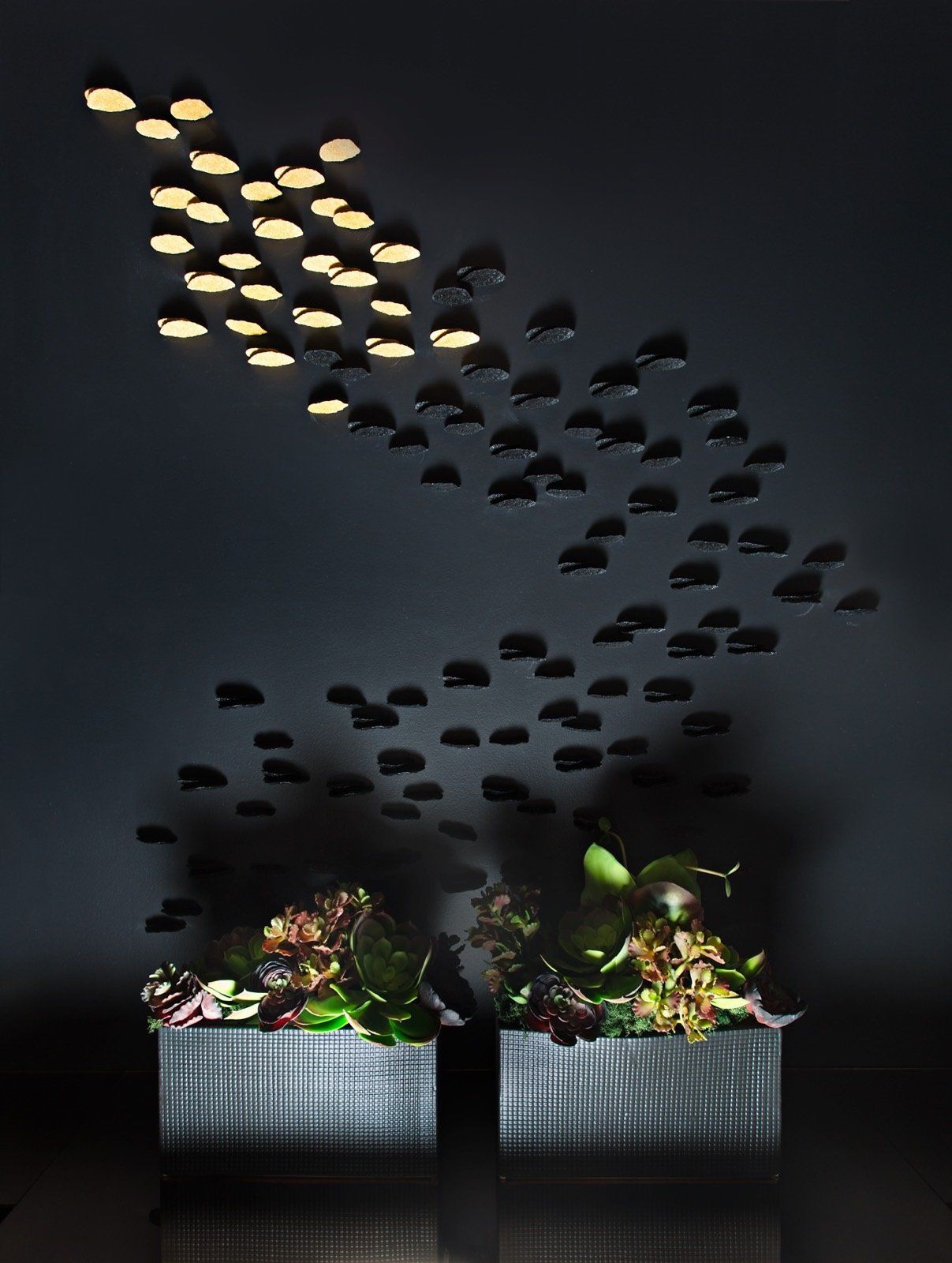 Two potted plants are sitting under a ceiling with a flock of fish on it