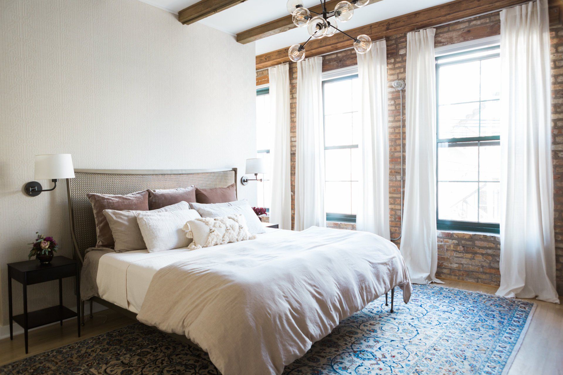 A bedroom with a bed , two windows , a rug and a brick wall.