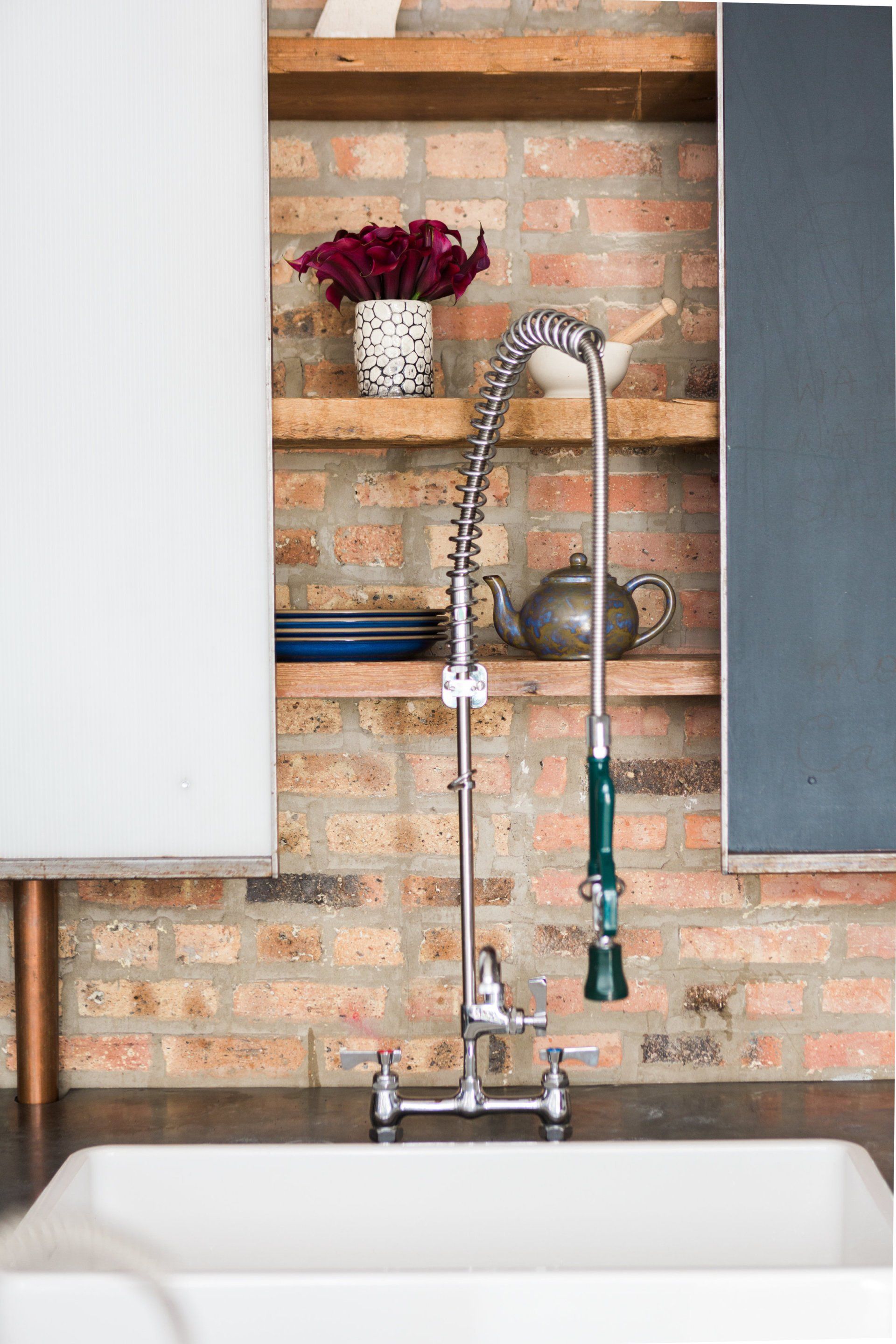 A kitchen sink with a faucet and a brick wall behind it.
