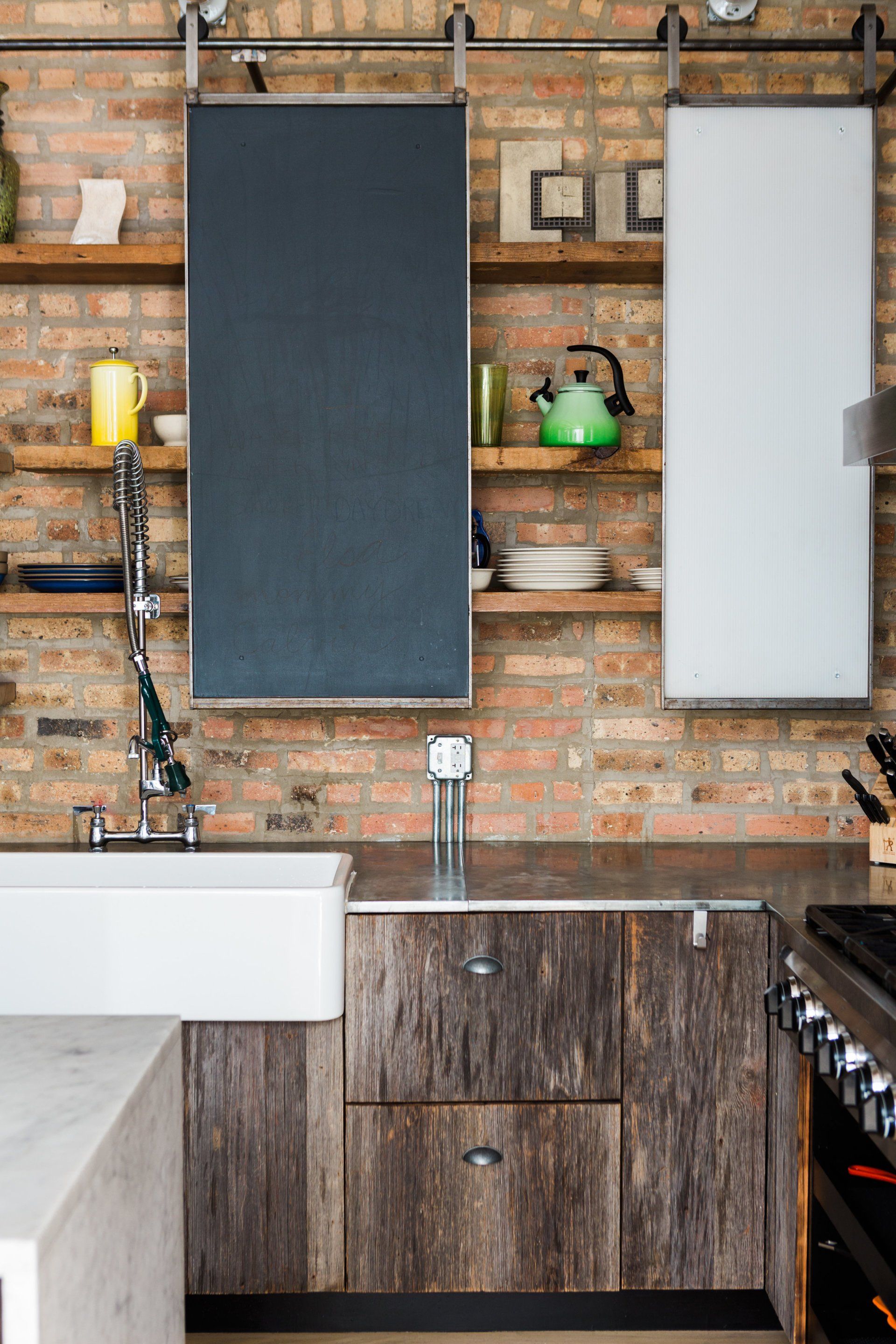 A kitchen with a sink , stove , chalkboard and shelves