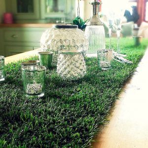 A table with a runner made of artificial grass and candles on it.