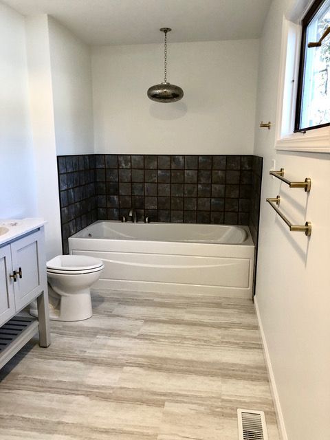 A bathroom with a tub , toilet , sink and window.