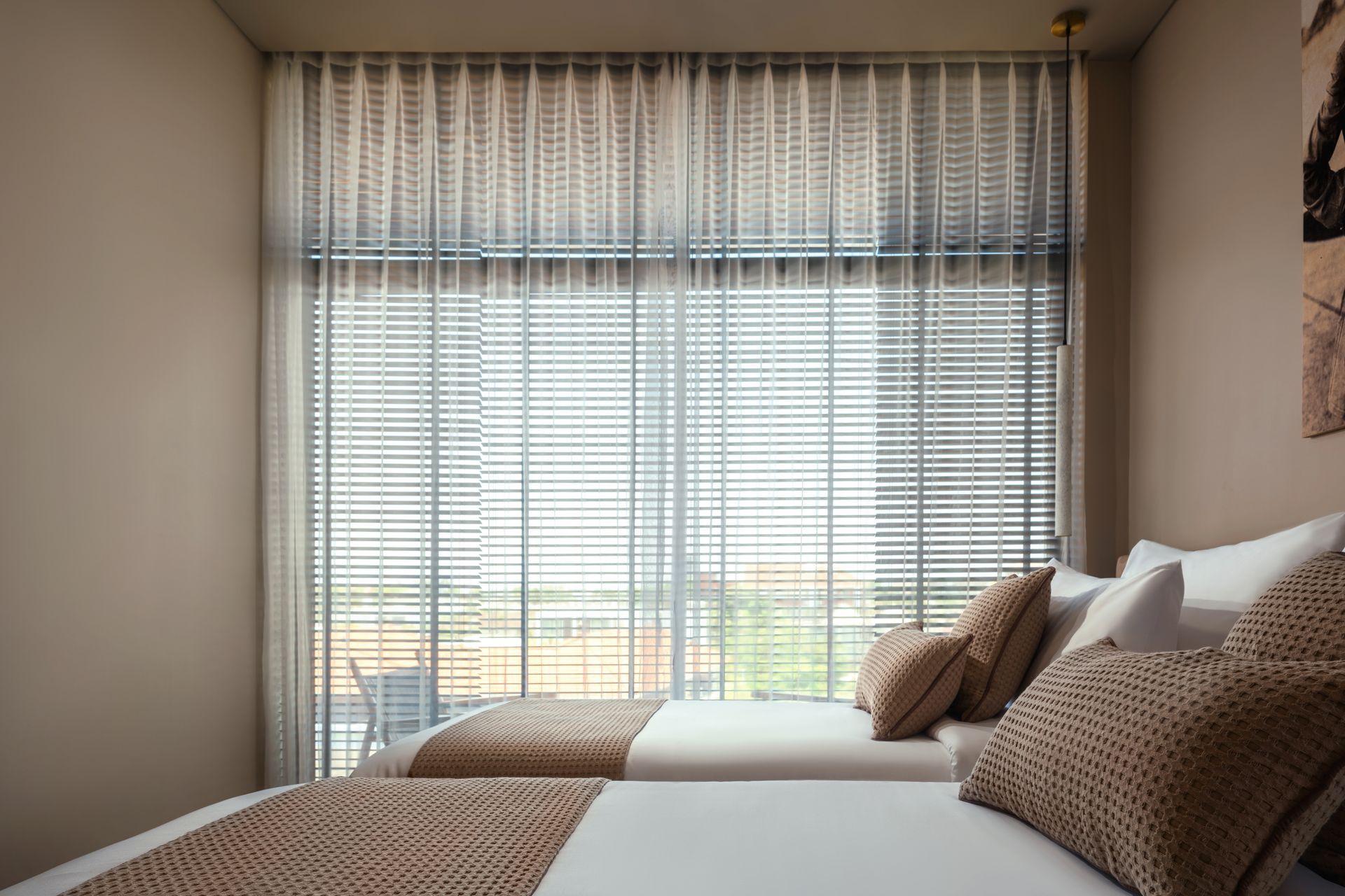 A bedroom with two beds and a large window with blinds.