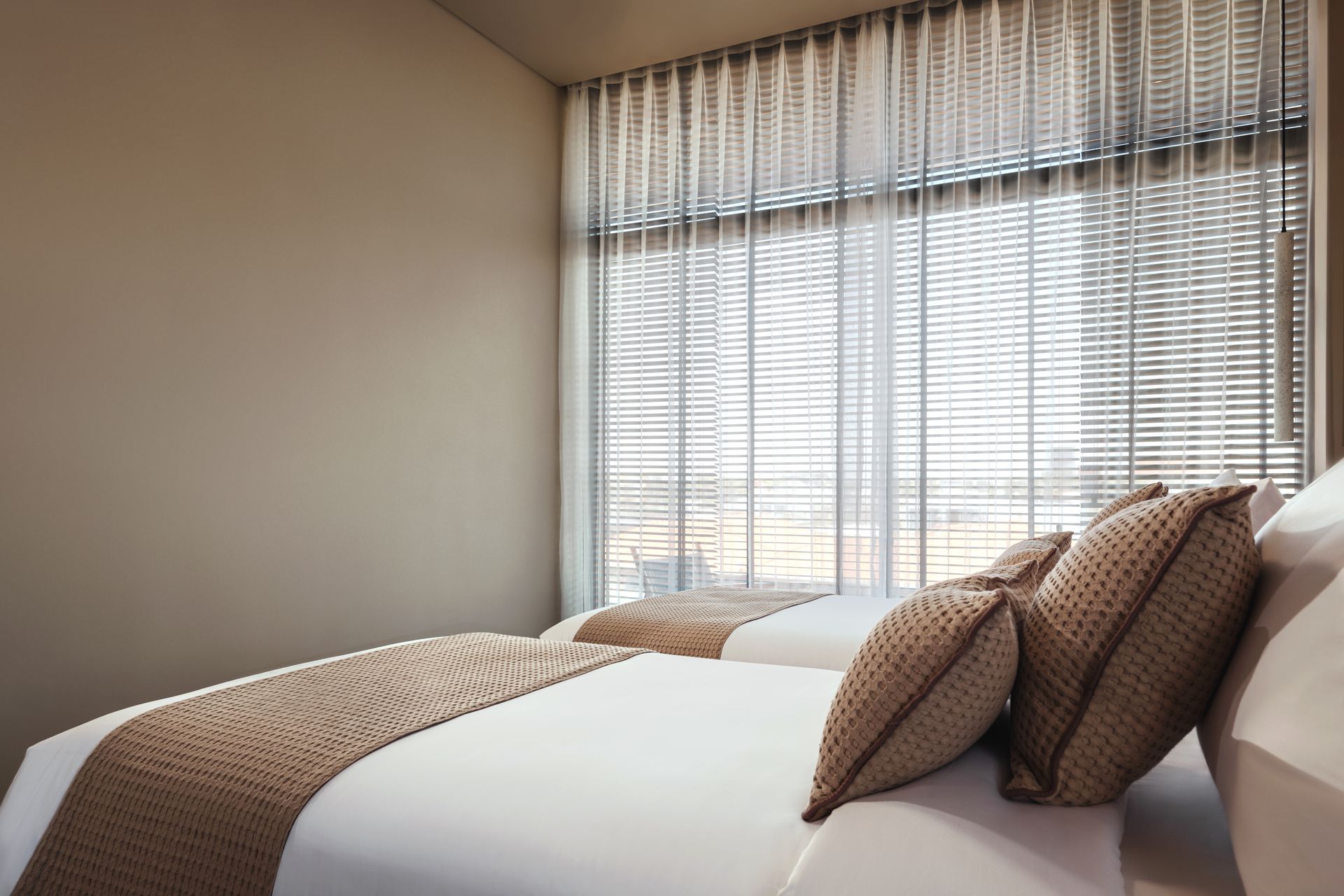 A bedroom with two beds and a large window with blinds.