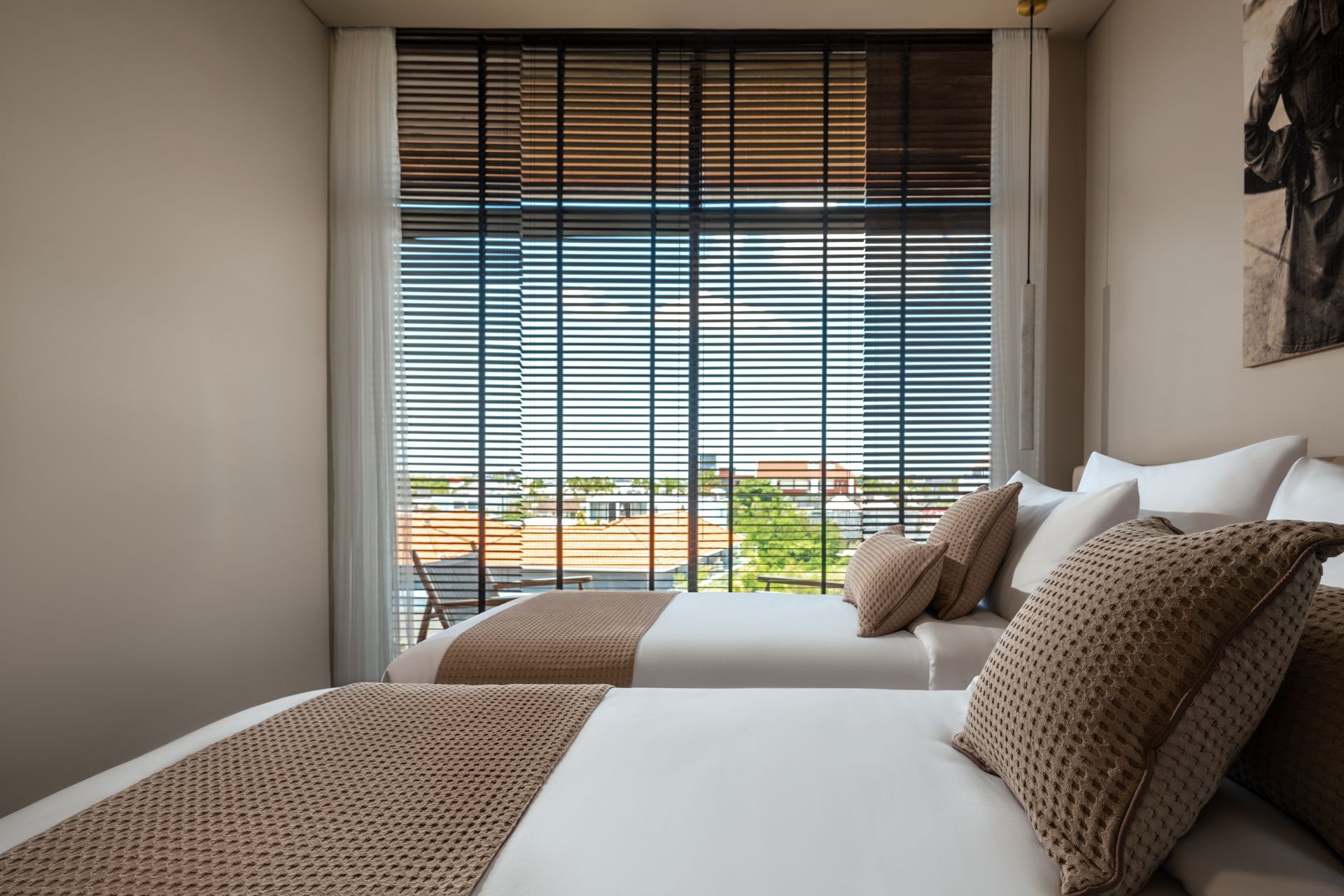 A bedroom with two beds and a large window with blinds.