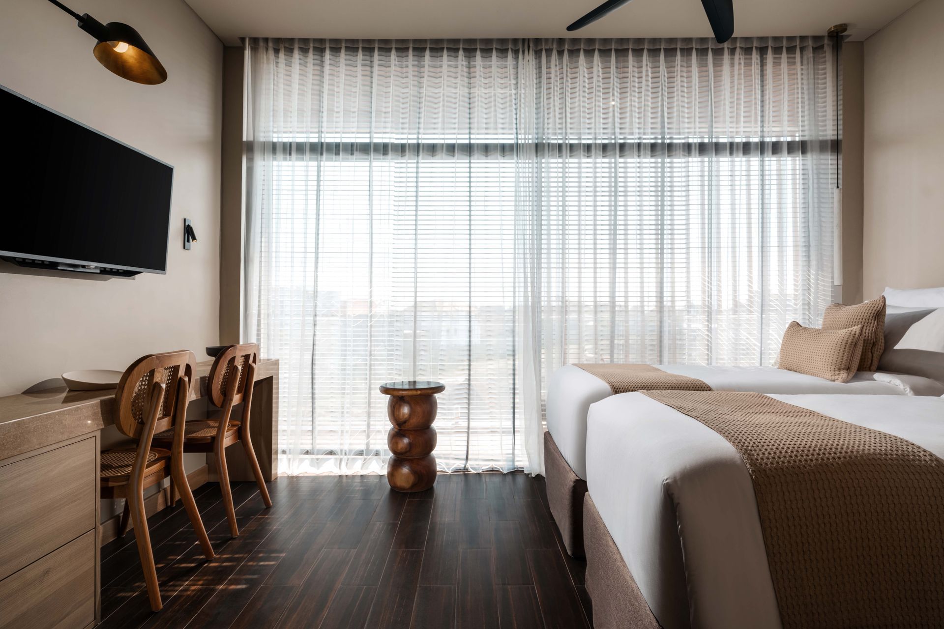 A hotel room with two beds , a desk , chairs and a flat screen tv.