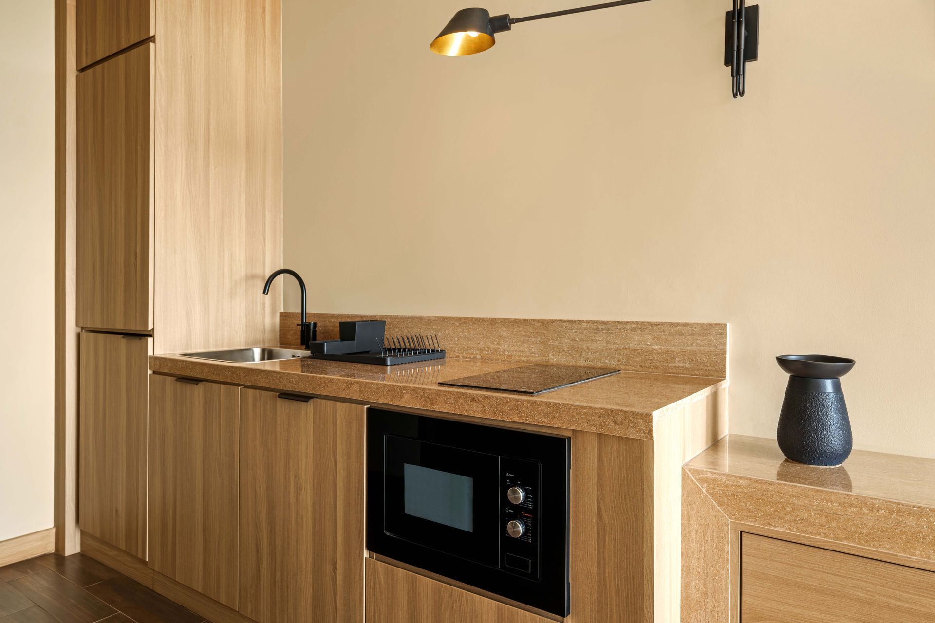 A kitchen with wooden cabinets , a microwave , a sink , and a lamp.