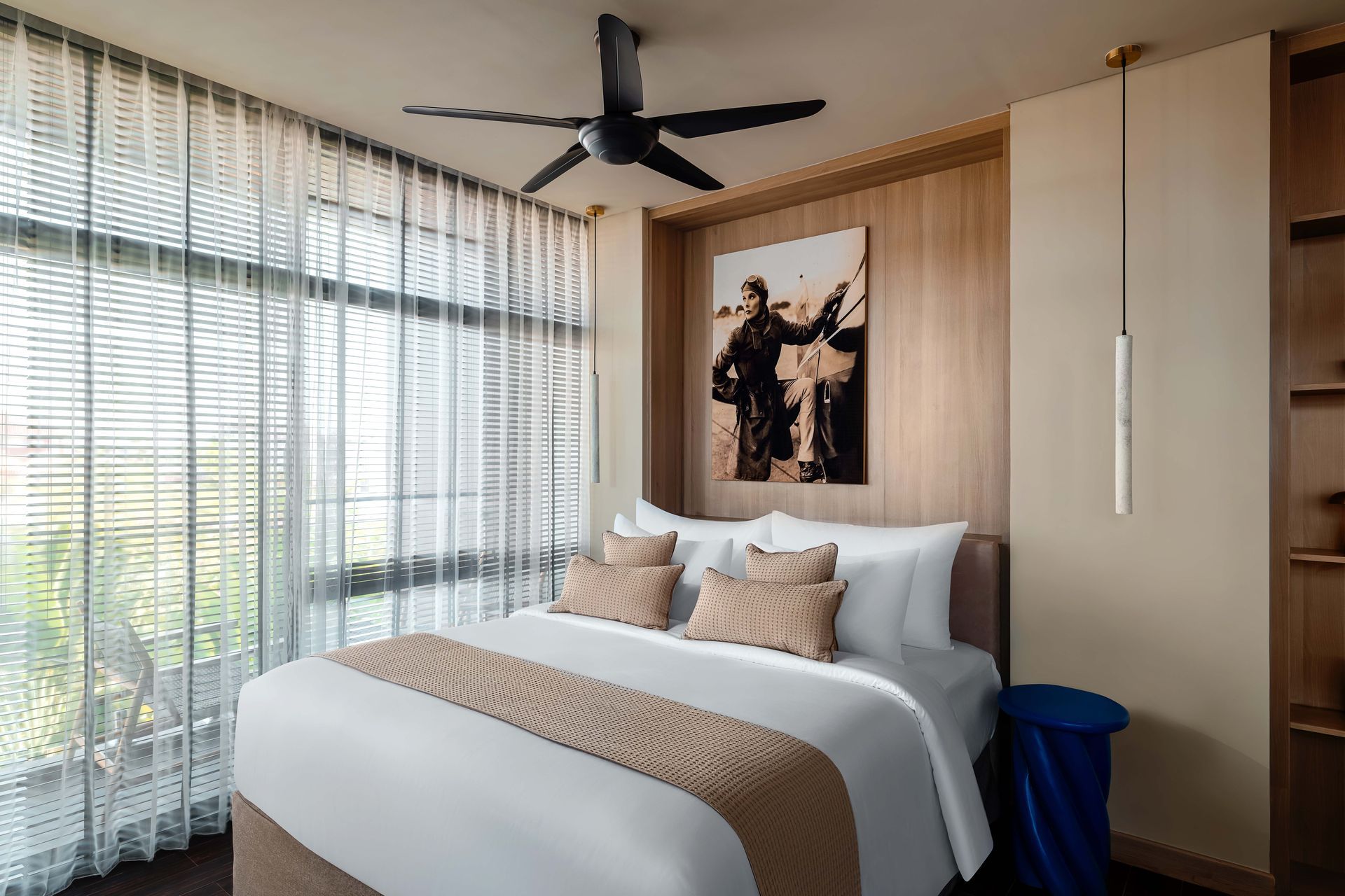 A bedroom with a large bed , a ceiling fan , and a painting on the wall.