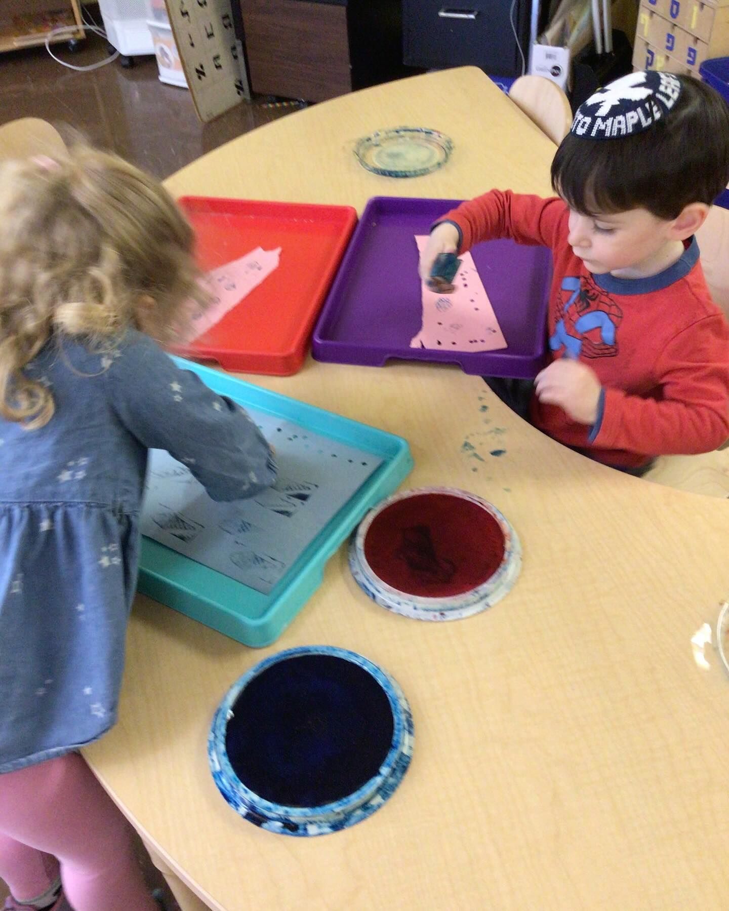 A boy and a girl are sitting at a table with trays of paint