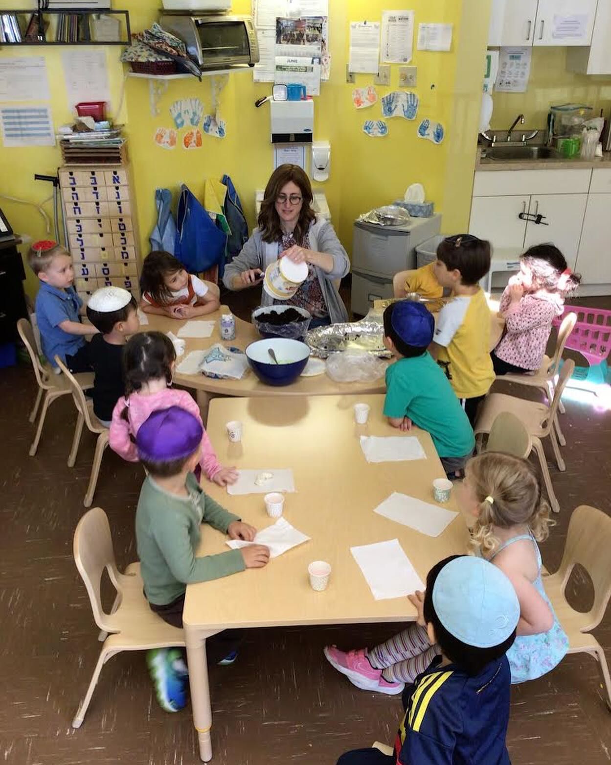 A group of children are sitting around a table with a teacher