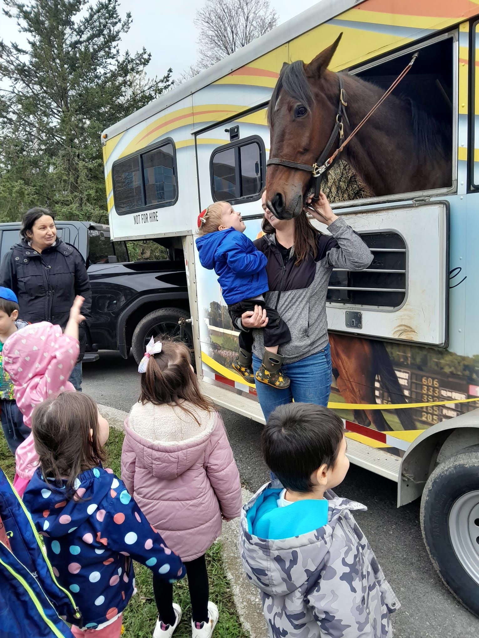 A group of children are standing in front of a horse trailer.