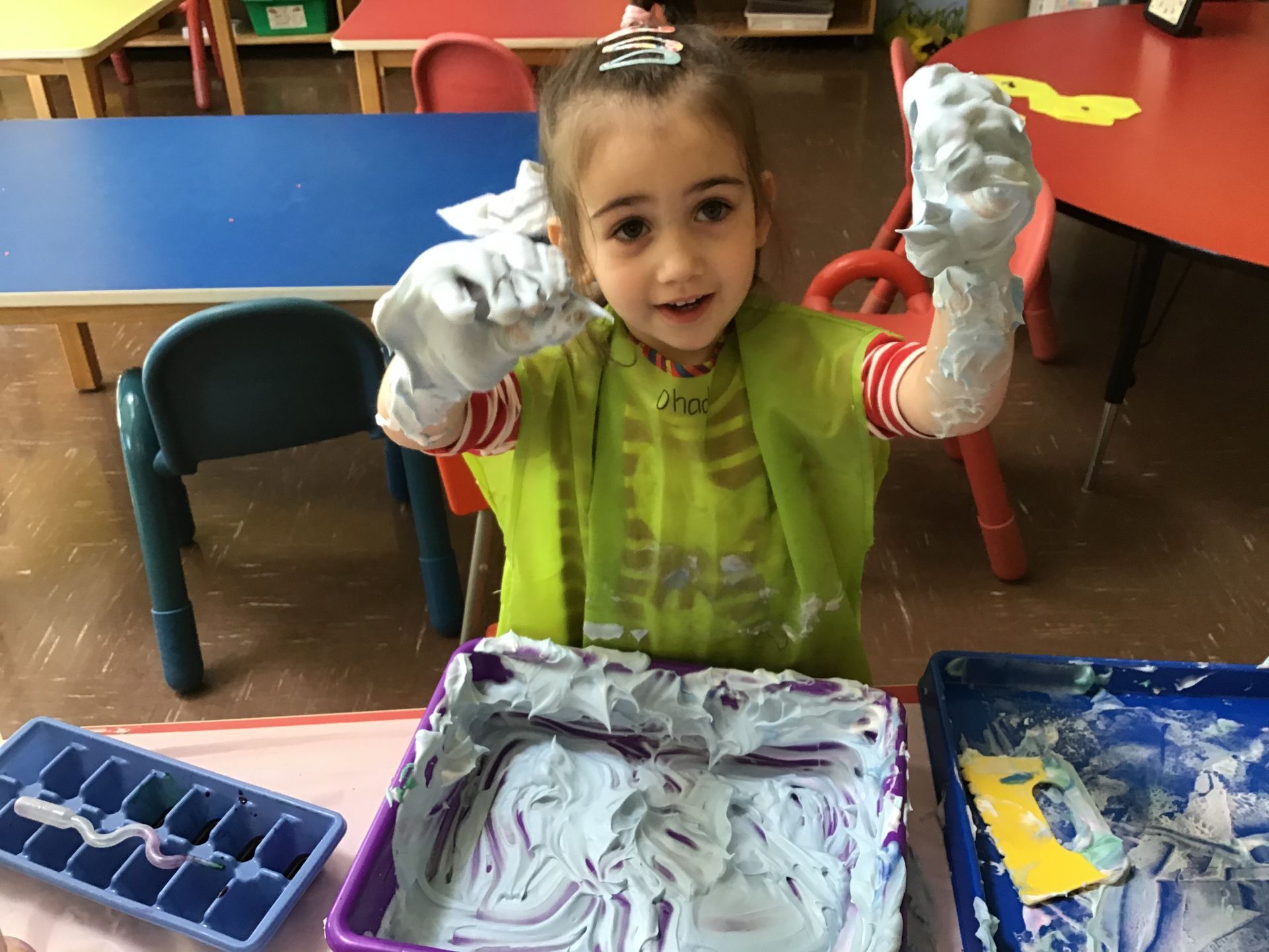 A little girl is playing with shaving cream in a classroom.