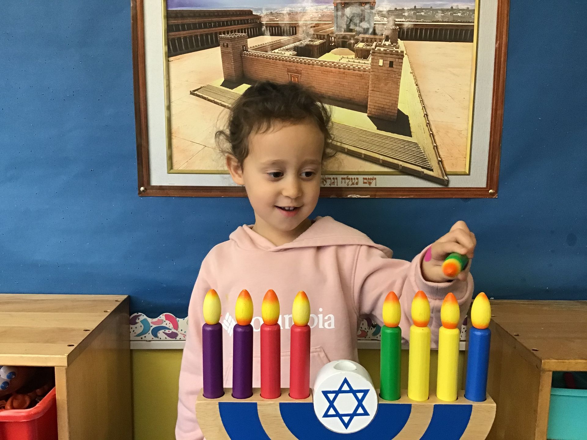 A little girl is playing with a menorah in front of a picture of a castle.