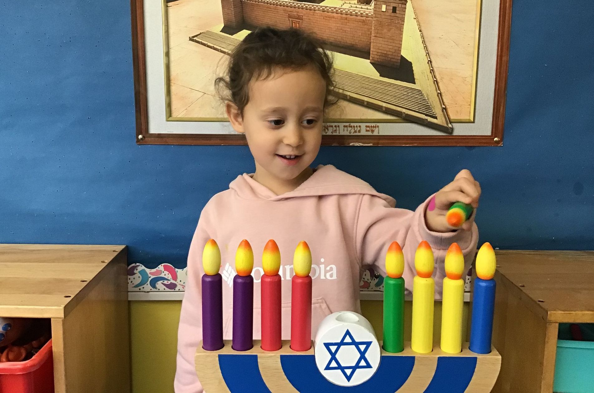 A little girl is playing with a menorah with candles