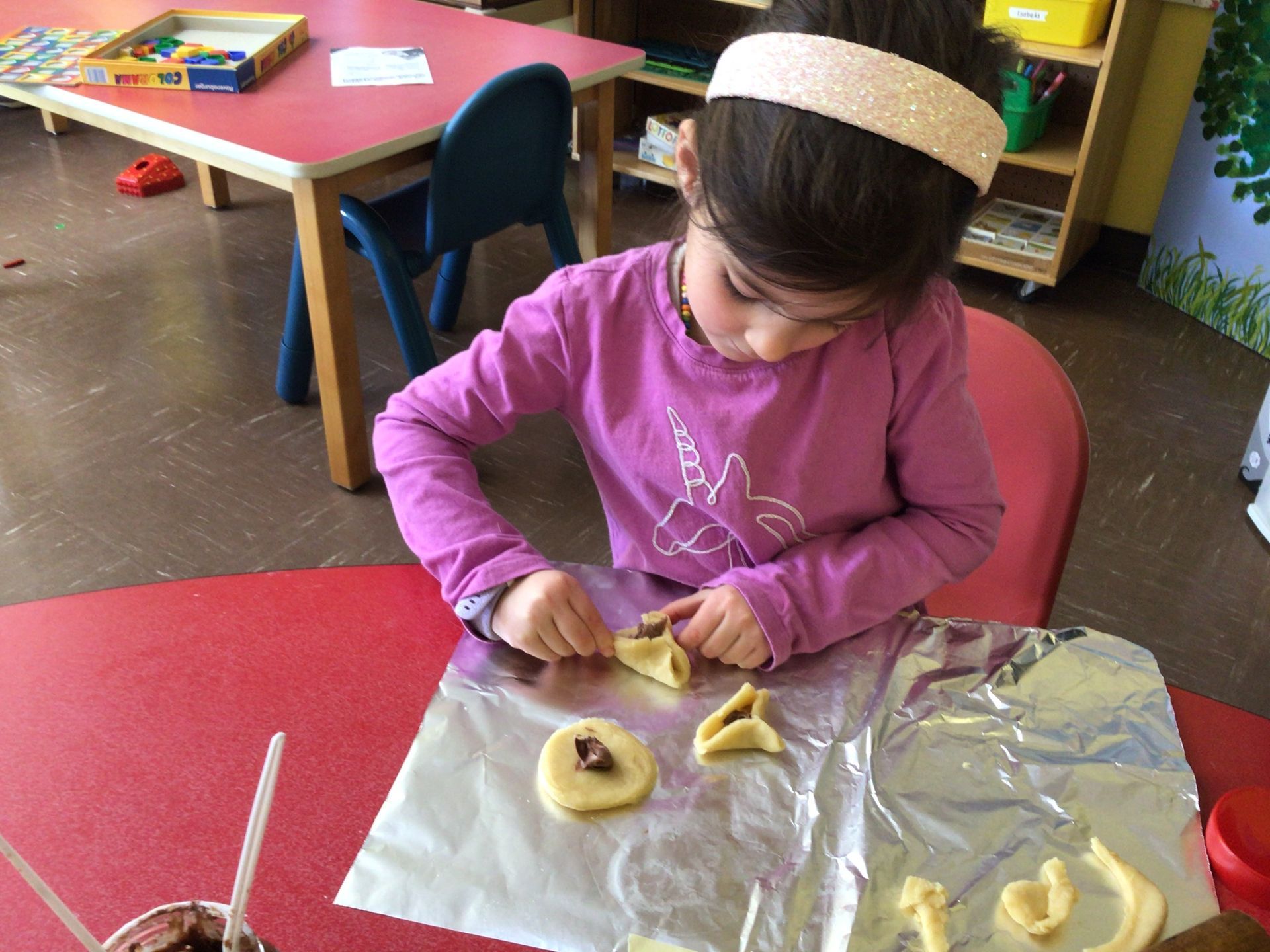 A little girl in a purple shirt is sitting at a table making cookies.