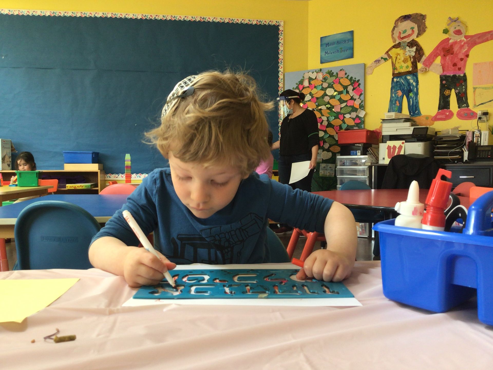 A young boy is sitting at a table in a classroom writing on a piece of paper