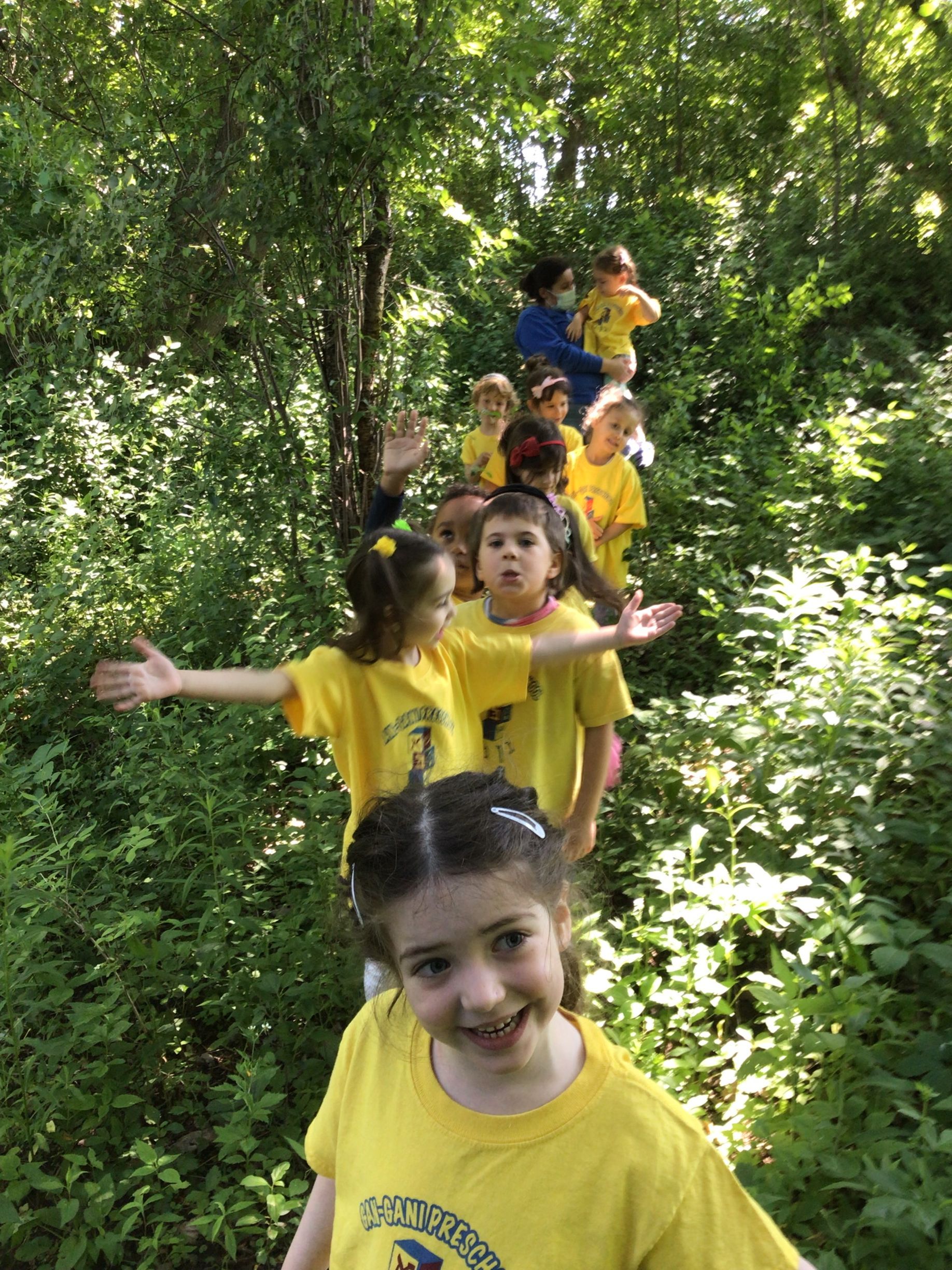 A group of children in yellow shirts are walking through the woods.