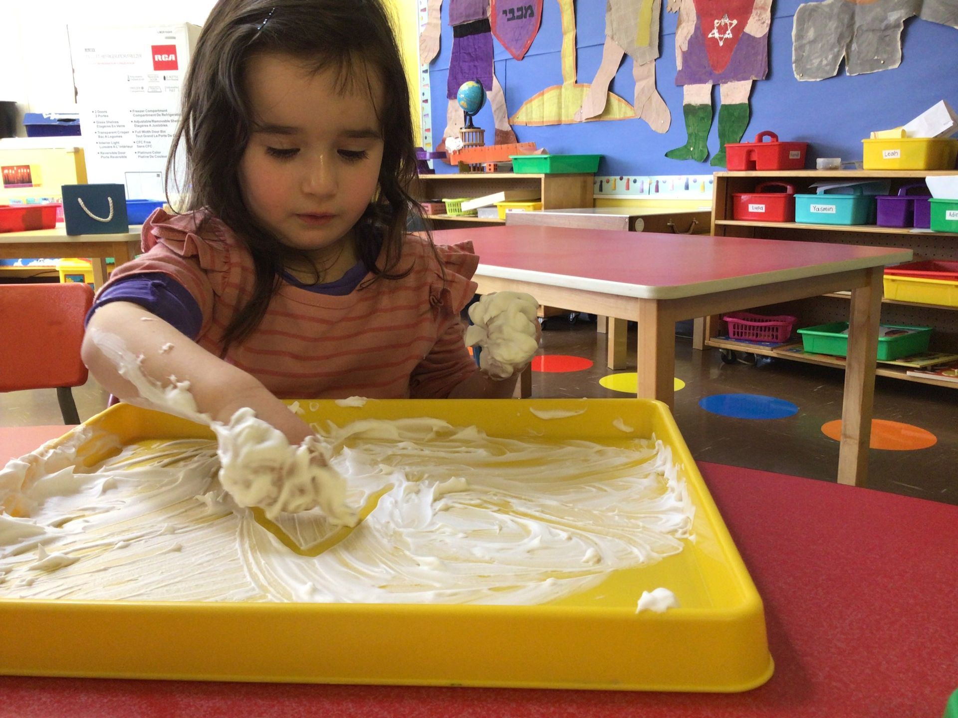 A little girl is playing with sand on a yellow tray