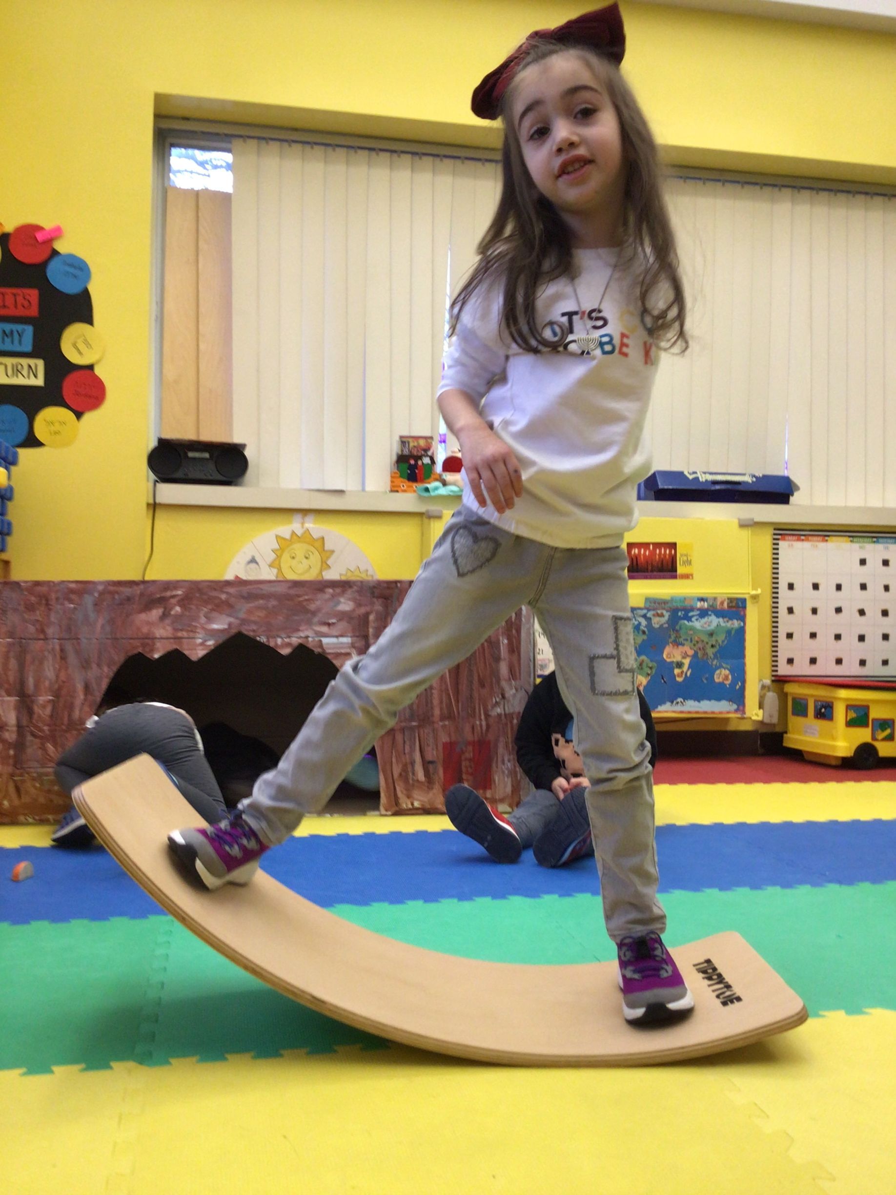 A little girl is standing on a wooden balance board