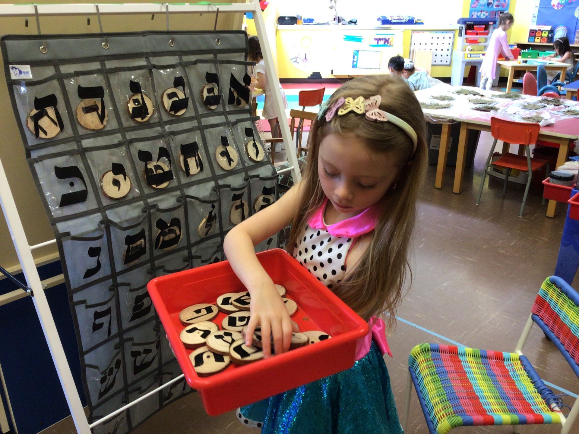 A little girl is playing with wooden letters in a classroom