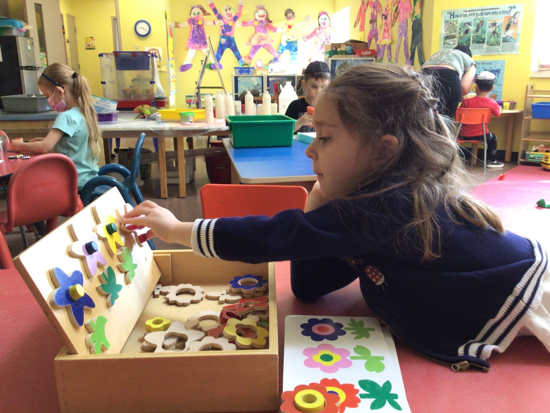 A little girl is playing with a wooden toy in a classroom.