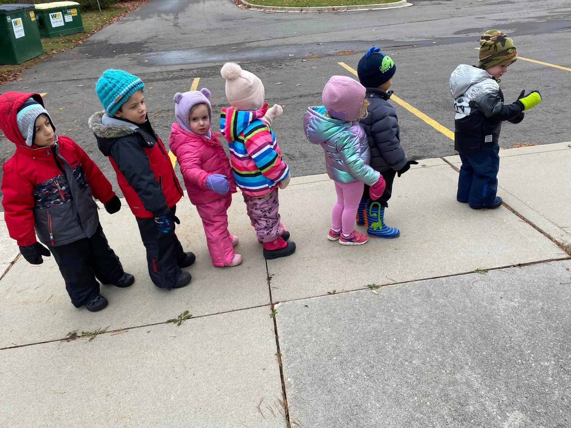 A group of children are standing on a sidewalk.
