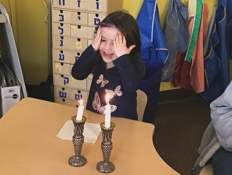 A little girl is sitting at a table with two lit candles