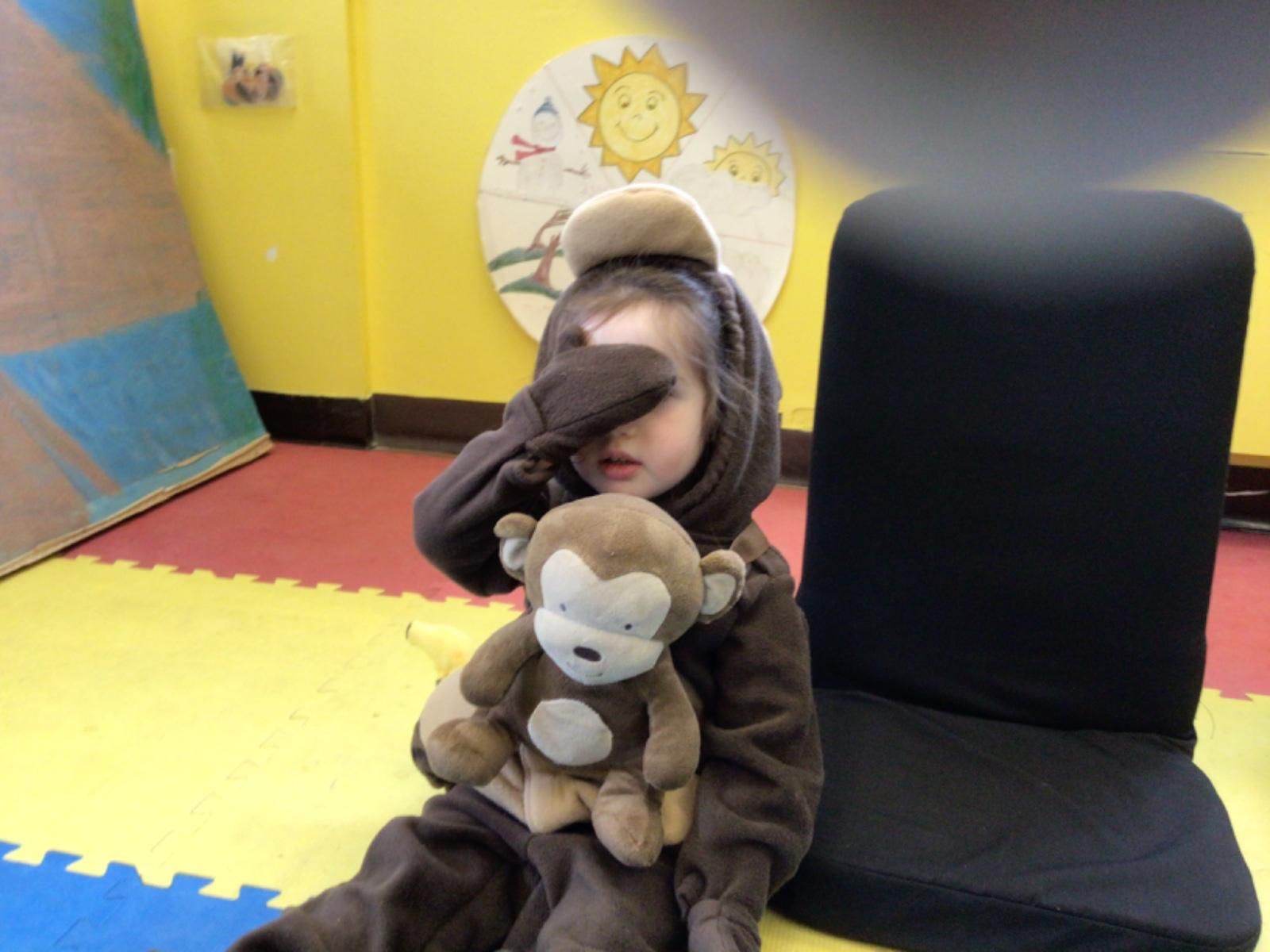 A child in a monkey costume holds a stuffed monkey