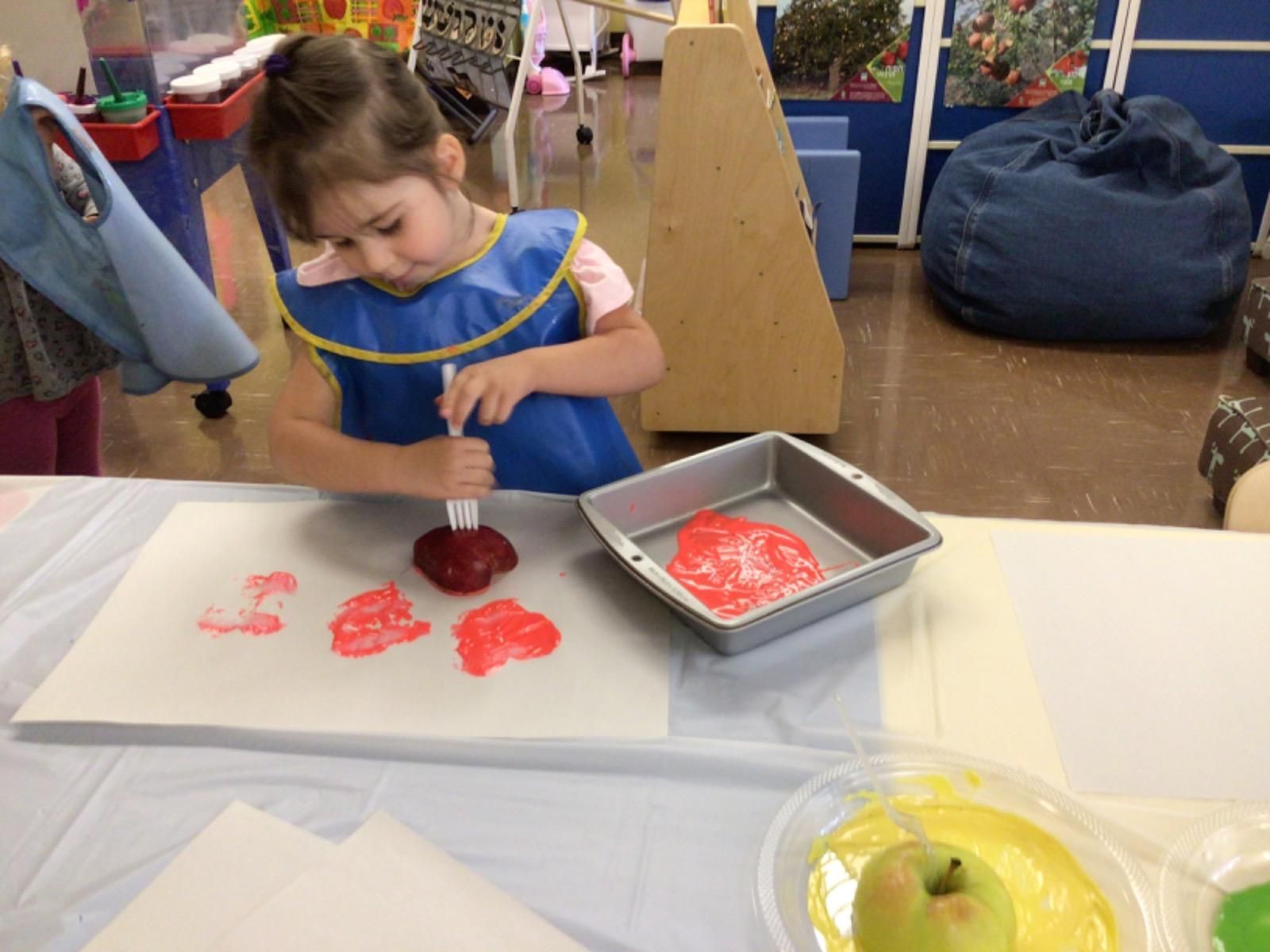 A little girl in a blue apron is painting on a piece of paper