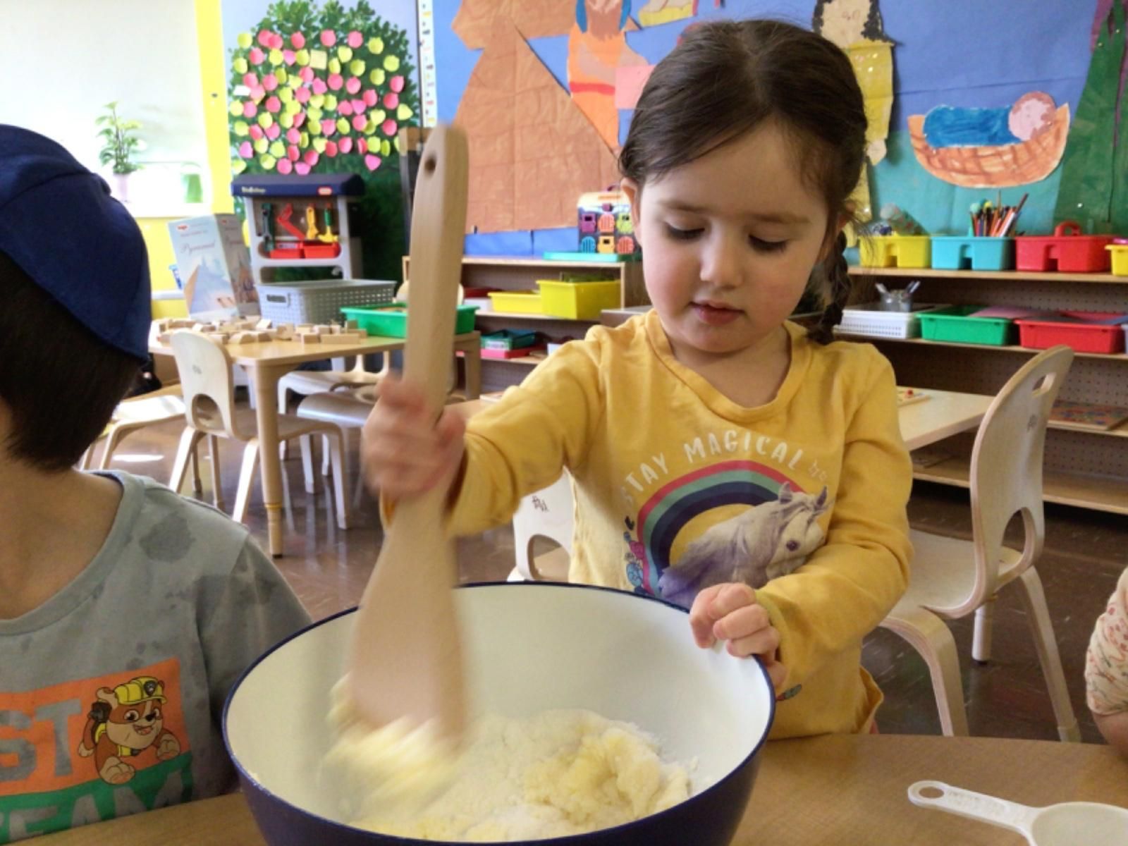 A little girl in a yellow shirt is mixing something in a bowl