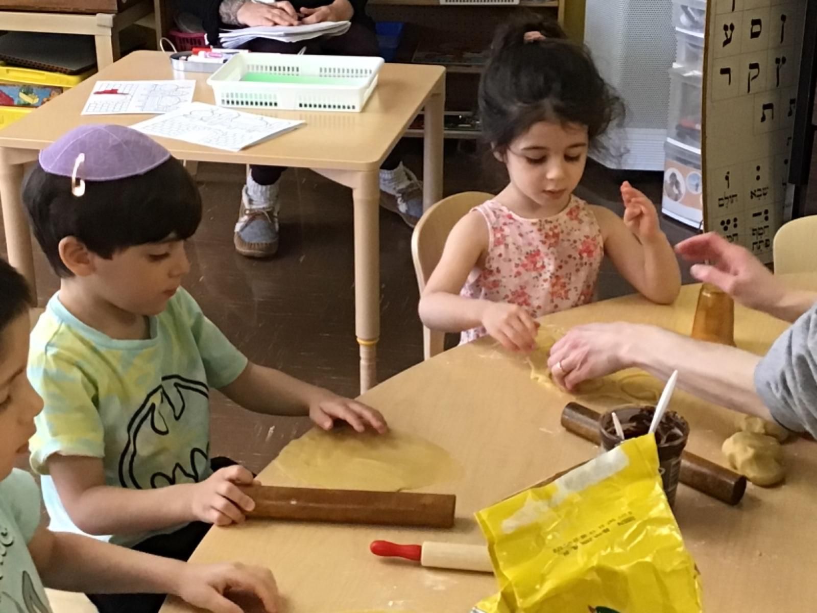 A group of children are sitting at a table with rolling pins and a bag of flour.