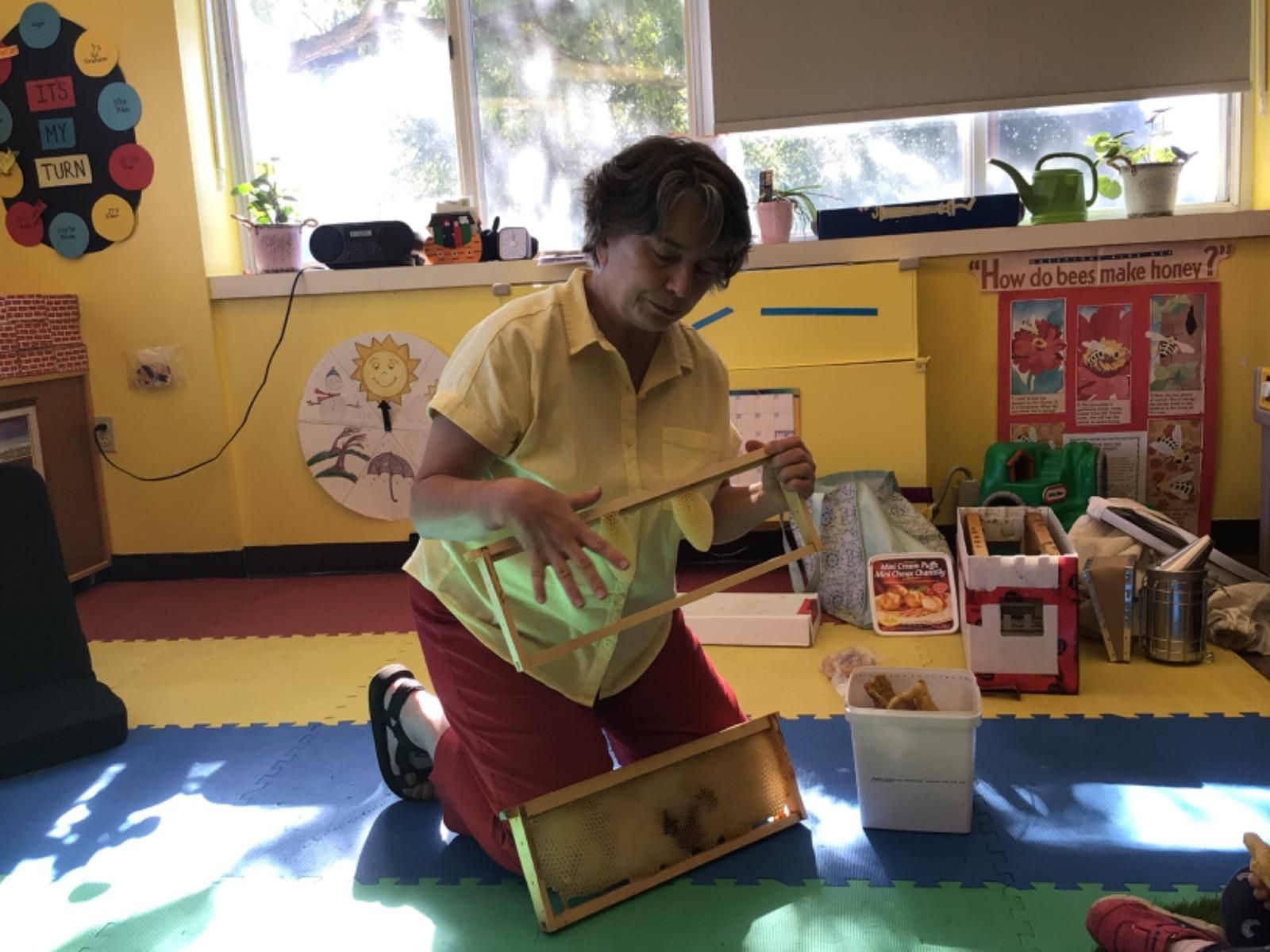 A woman in a yellow shirt is kneeling on the floor holding a wooden box.
